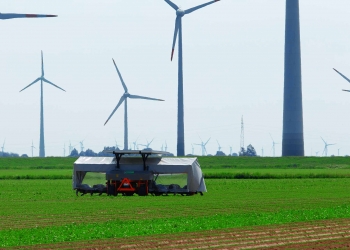 Agriculture - solar powered weeding machine in the fields, with wind turbines in the background